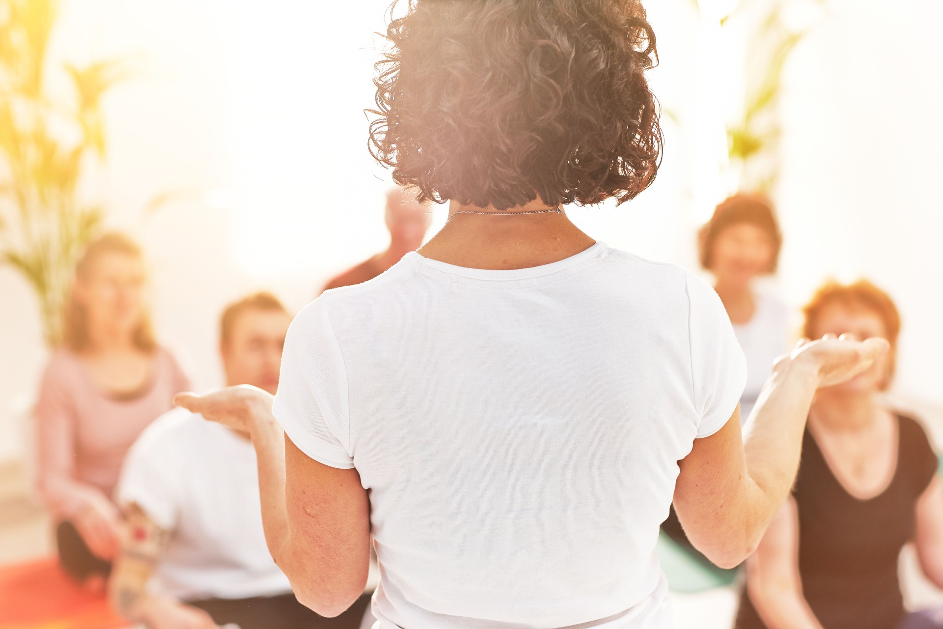 Rear view of a yoga instructor giving a lesson to a class in a health and wellness center. Female teacher giving an instructional lesson on meditation techniques to her students in a meditating class